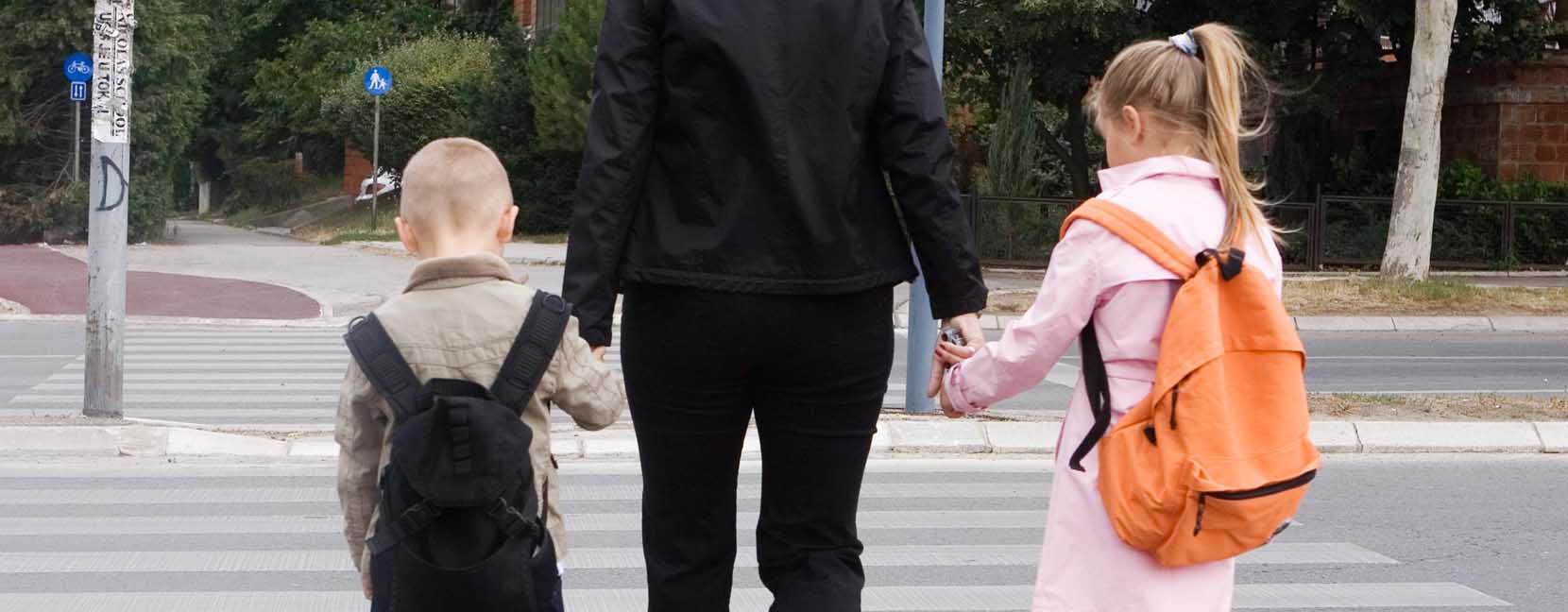 Mamma attraversa la strada tenendo per mano i suoi bambini