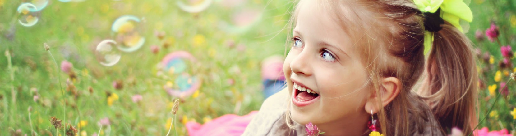 Bambina distesa in un prato che sorride in mezzo alle bolle di sapone