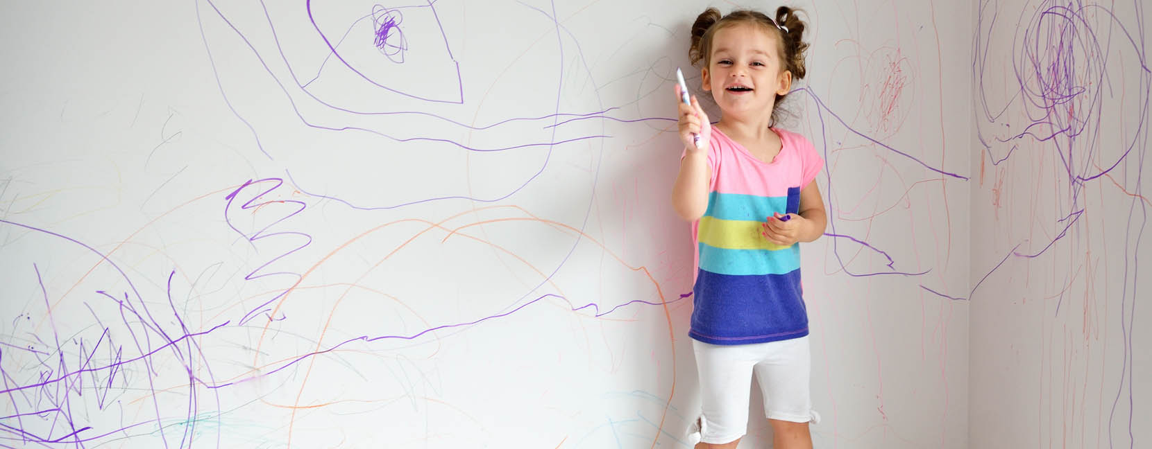 Bambina che ha disegnato con i pennarelli il muro e ride divertita