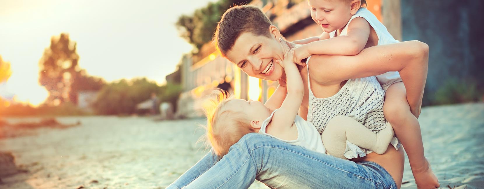 Mamma sorridente seduta con un bambino in braccio e l'altro sulla schiena: giocano