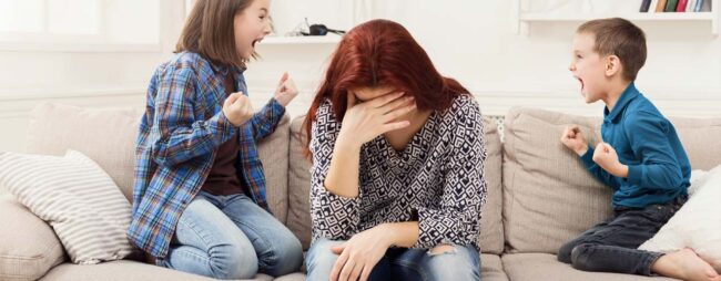 Le 5 cause genitore insicuro_1280x500 Una mamma demoralizzata seduta sul divano tra i figli che "cantano vittoria", mamma insicura