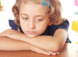Bambina si appoggia alla scrivania annoiata tra pile di libri, odia i compiti