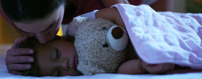 Mamma da il bacio della buonanotte alla sua bimba addormentata